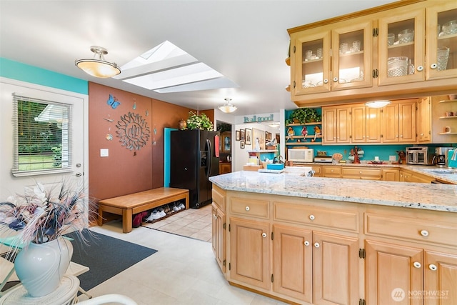 kitchen featuring light stone counters, light brown cabinetry, black refrigerator with ice dispenser, and a skylight