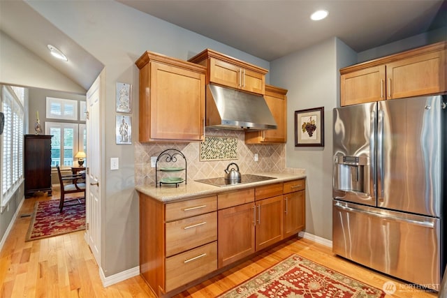 kitchen featuring light hardwood / wood-style floors, black electric stovetop, stainless steel fridge, and tasteful backsplash