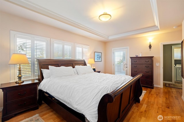 bedroom with light wood-type flooring, ornamental molding, a tray ceiling, and washer / clothes dryer