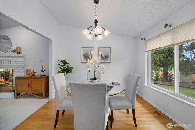 dining space with a textured ceiling, light wood-type flooring, a fireplace, and visible vents