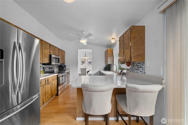 kitchen with a peninsula, brown cabinetry, appliances with stainless steel finishes, and a breakfast bar