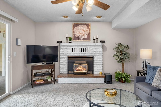 carpeted living room with a textured ceiling, ceiling fan, a fireplace, and baseboards