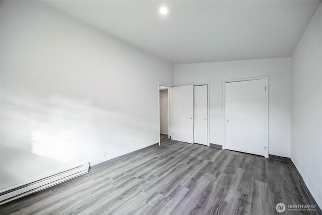 unfurnished bedroom with wood-type flooring, a baseboard radiator, and two closets