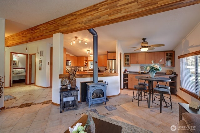 living area with ceiling fan, a wood stove, vaulted ceiling with beams, and light tile patterned floors