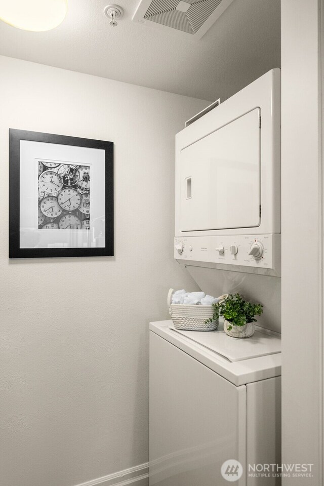 laundry area with stacked washer and clothes dryer, visible vents, baseboards, and laundry area