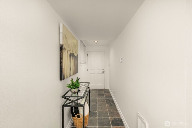 hallway featuring stone finish floor, visible vents, and baseboards