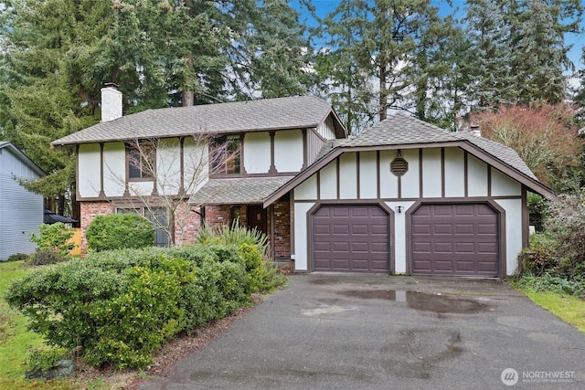 tudor house with a garage, driveway, a chimney, roof with shingles, and brick siding