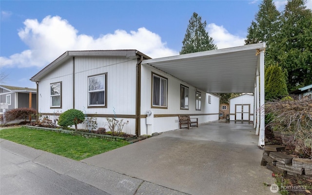 view of side of property with a storage unit, an attached carport, concrete driveway, and an outbuilding