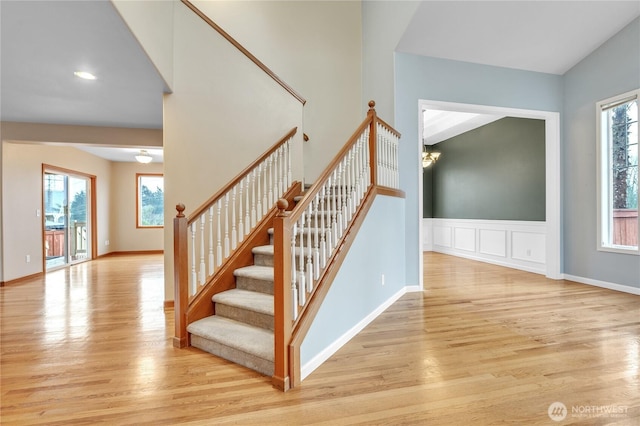 stairs featuring baseboards, a decorative wall, wood finished floors, and wainscoting