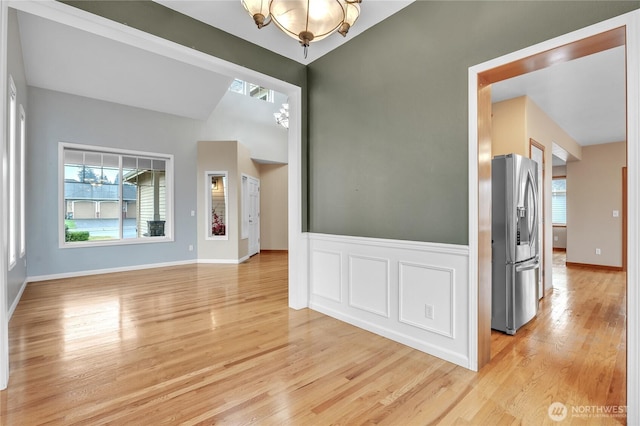 unfurnished room with light wood-type flooring, a decorative wall, and wainscoting