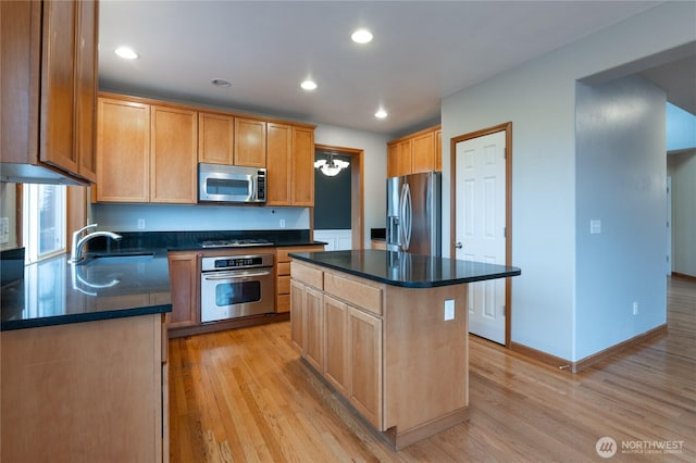 kitchen featuring dark countertops, light wood finished floors, a kitchen island, and appliances with stainless steel finishes