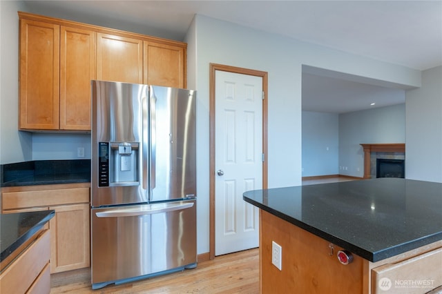 kitchen featuring a fireplace, light wood-style floors, stainless steel fridge with ice dispenser, a center island, and dark stone counters