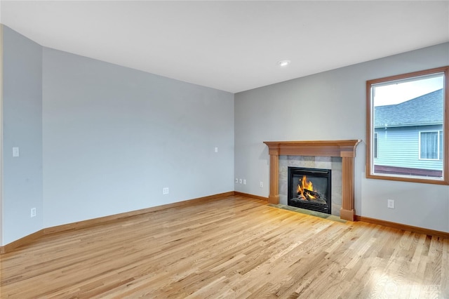 unfurnished living room with a tile fireplace, baseboards, and light wood finished floors