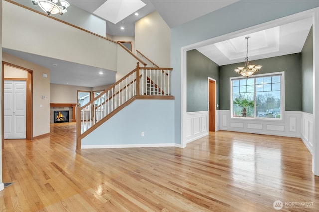 interior space with light wood finished floors, a tiled fireplace, stairs, a chandelier, and a decorative wall