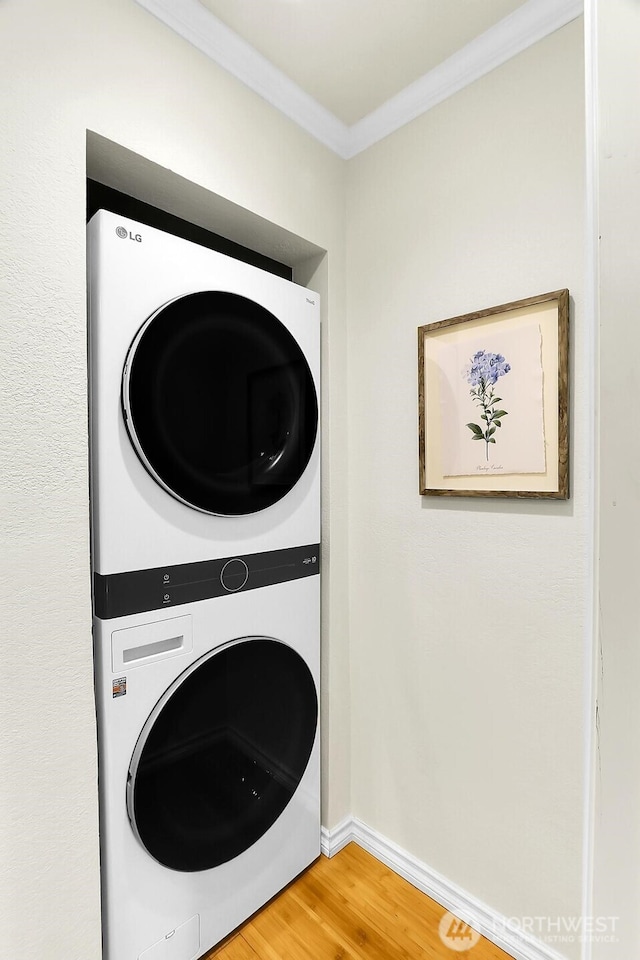 washroom with laundry area, baseboards, stacked washer / dryer, ornamental molding, and wood finished floors