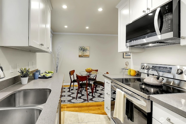 kitchen with stainless steel appliances, crown molding, a sink, and white cabinetry