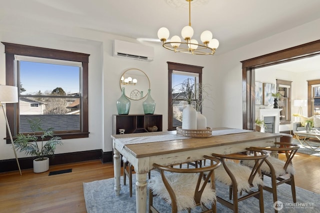 dining space with a wall unit AC, a chandelier, and light wood-type flooring