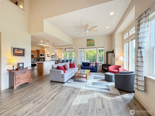 living room with light wood-style flooring, recessed lighting, baseboards, ceiling fan, and a wood stove