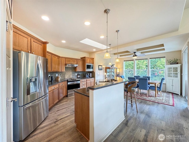 kitchen with dark countertops, wood finished floors, brown cabinets, and stainless steel appliances