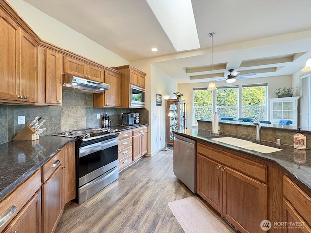 kitchen featuring a skylight, a sink, stainless steel appliances, under cabinet range hood, and brown cabinets