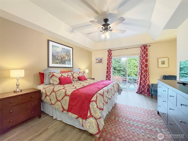 bedroom with access to exterior, light wood-style floors, and a tray ceiling