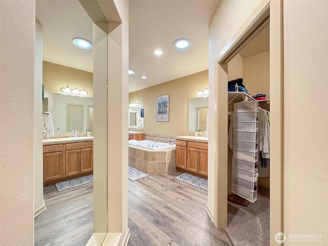 bathroom with a garden tub, a spacious closet, two vanities, and wood finished floors