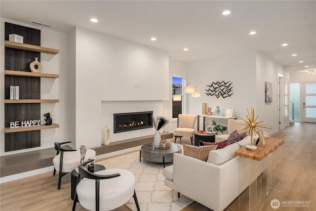 living room featuring baseboards, visible vents, a glass covered fireplace, wood finished floors, and recessed lighting