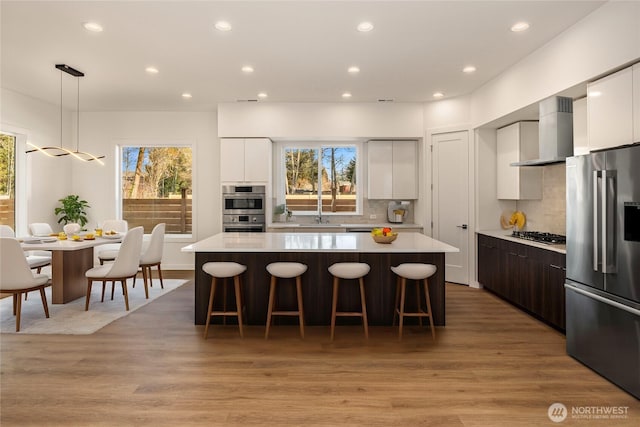 kitchen with stainless steel appliances, a kitchen breakfast bar, a center island, wall chimney exhaust hood, and modern cabinets