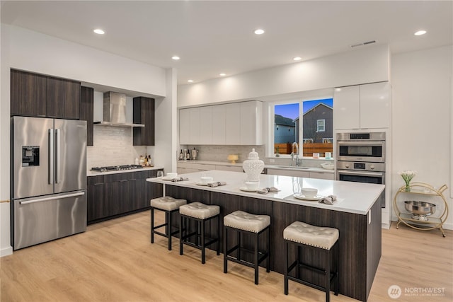 kitchen featuring stainless steel appliances, visible vents, a sink, wall chimney range hood, and modern cabinets