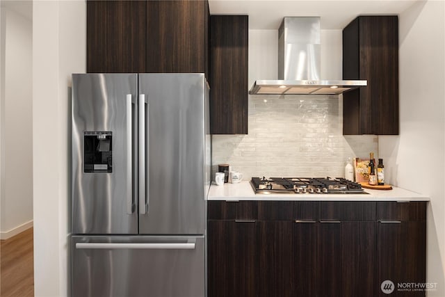 kitchen featuring modern cabinets, stainless steel appliances, dark brown cabinets, wall chimney range hood, and backsplash