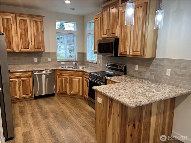 kitchen with light wood-type flooring, stainless steel appliances, decorative light fixtures, sink, and light stone counters