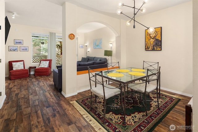 dining area featuring arched walkways, a notable chandelier, wood finished floors, and baseboards