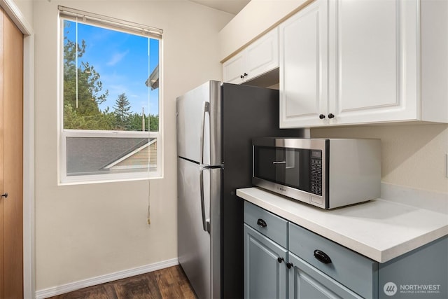 kitchen with baseboards, white cabinets, stainless steel microwave, light countertops, and gray cabinetry