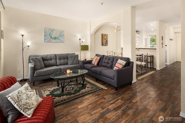 living area featuring arched walkways, wood finished floors, and baseboards