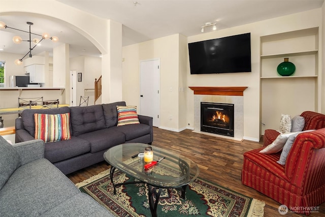 living room featuring a chandelier, a tile fireplace, baseboards, and wood finished floors