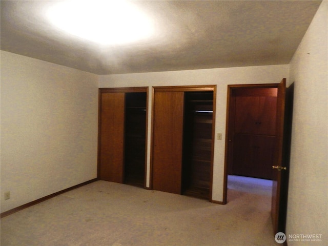 unfurnished bedroom featuring light carpet and two closets