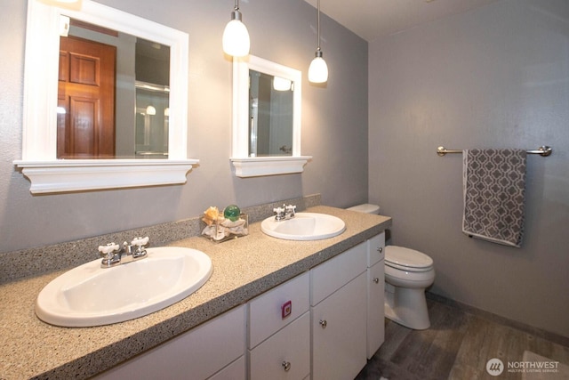 bathroom with double vanity, wood finished floors, a sink, and toilet