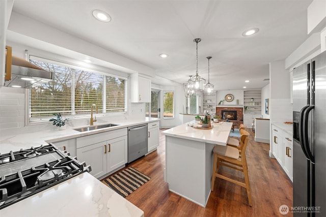 kitchen with stainless steel appliances, a sink, white cabinetry, a kitchen breakfast bar, and a center island