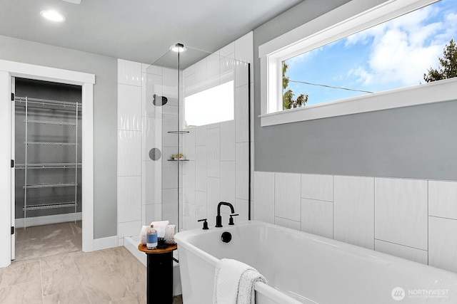 bathroom featuring a walk in closet, marble finish floor, a soaking tub, a walk in shower, and baseboards