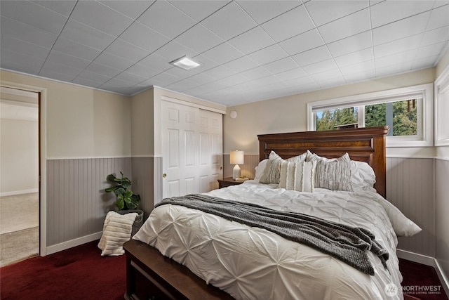 bedroom with a wainscoted wall, wood walls, a closet, and dark carpet