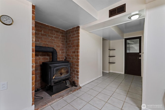 unfurnished living room with a wood stove, baseboards, visible vents, and light tile patterned flooring