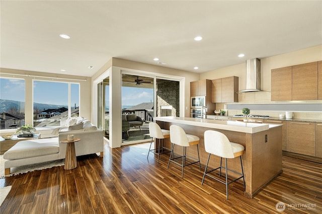 kitchen featuring appliances with stainless steel finishes, a mountain view, an island with sink, wall chimney range hood, and a breakfast bar