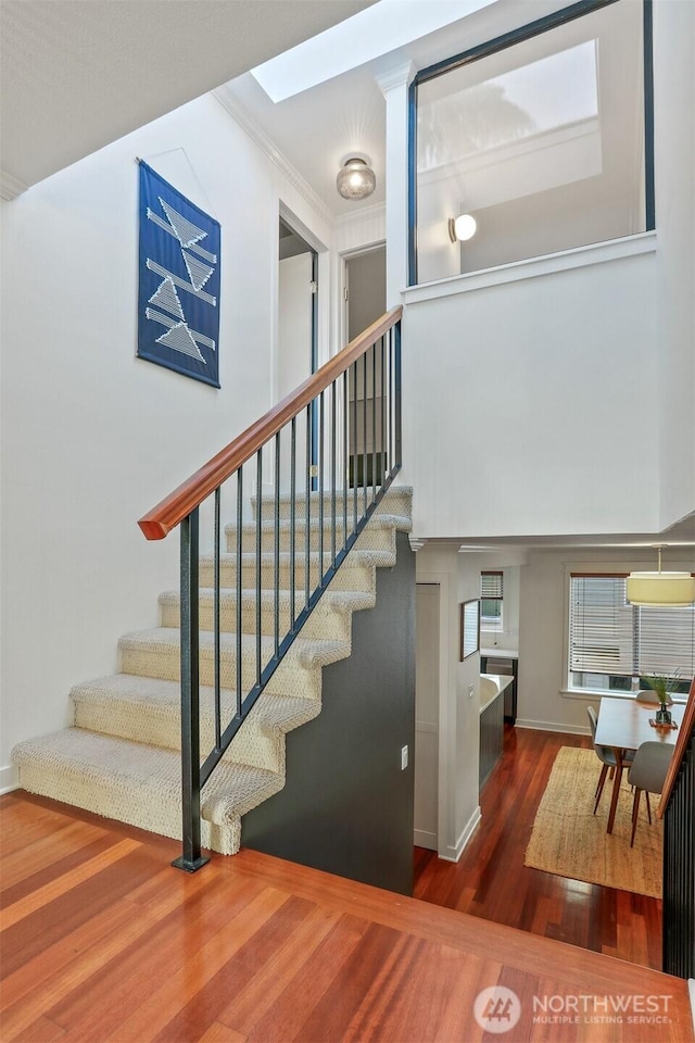 stairway with a high ceiling, a skylight, wood finished floors, and baseboards