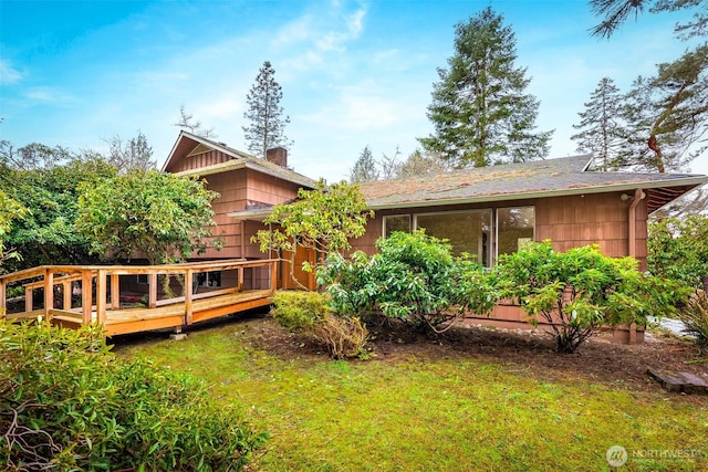 back of property featuring a lawn, a chimney, and a wooden deck