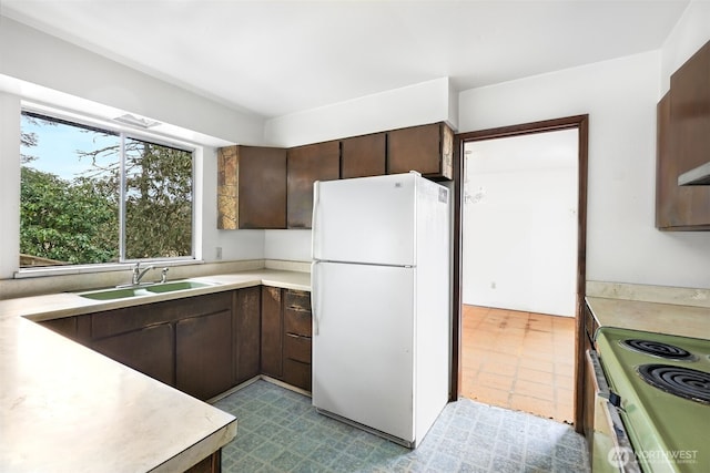 kitchen featuring freestanding refrigerator, light countertops, a sink, and dark brown cabinets