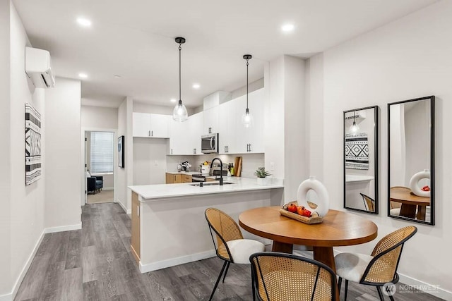 kitchen with wood-type flooring, stainless steel appliances, a wall mounted AC, white cabinetry, and kitchen peninsula