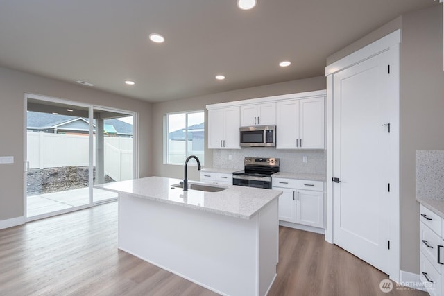 kitchen featuring a kitchen island with sink, stainless steel appliances, a sink, white cabinets, and light stone countertops