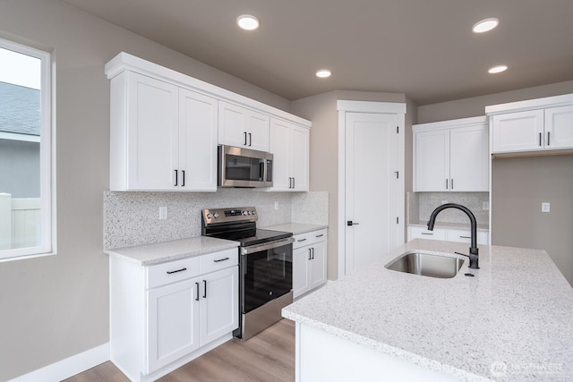 kitchen featuring light stone countertops, white cabinetry, stainless steel appliances, and a sink