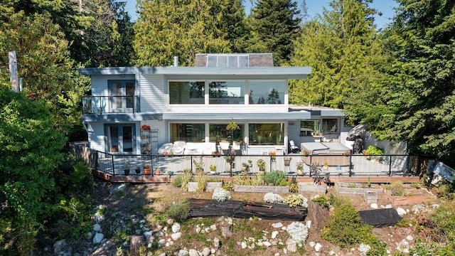 back of property featuring a garden, a balcony, and a wooden deck