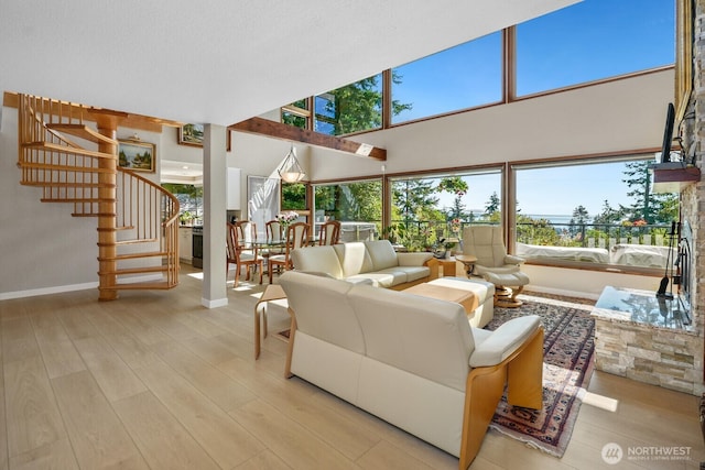 living area with light wood-type flooring, baseboards, stairway, and a towering ceiling